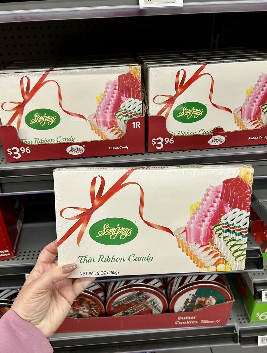 Hand holding vintage Christmas thin ribbon candy box with red bow, displayed among nostalgic holiday decorations on a store shelf.