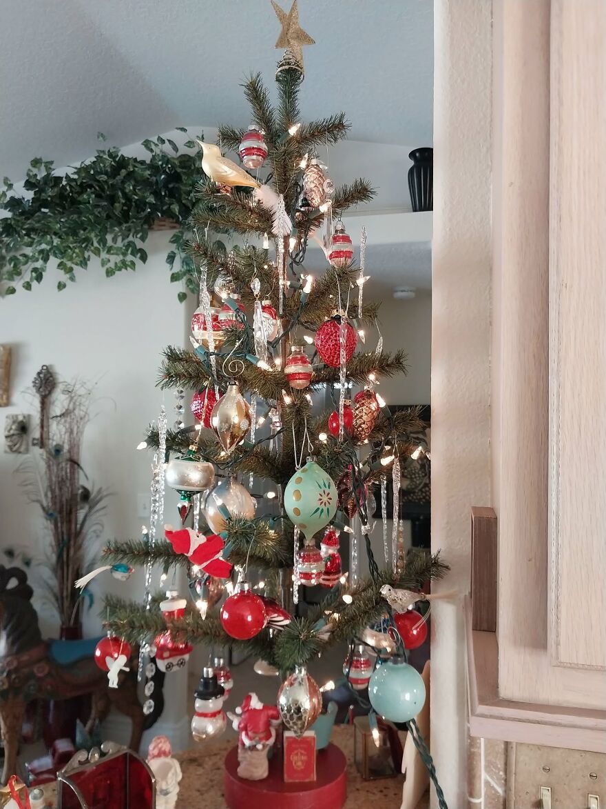 Vintage Christmas decorations on a tree featuring nostalgic red, gold, and blue ornaments with lights in a cozy home setting