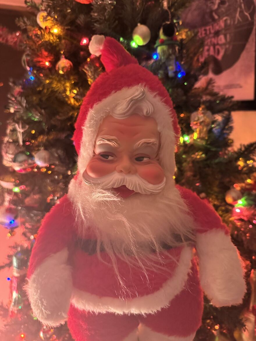 Vintage Christmas decoration of a classic Santa Claus figure in front of a decorated and lit Christmas tree.