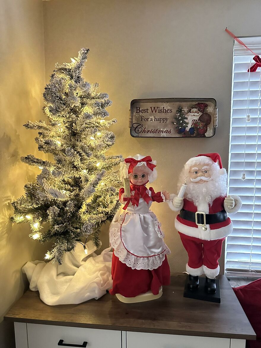 Vintage Christmas decorations featuring a lit snowy tree and classic Santa and Mrs. Claus figures on a wooden surface.