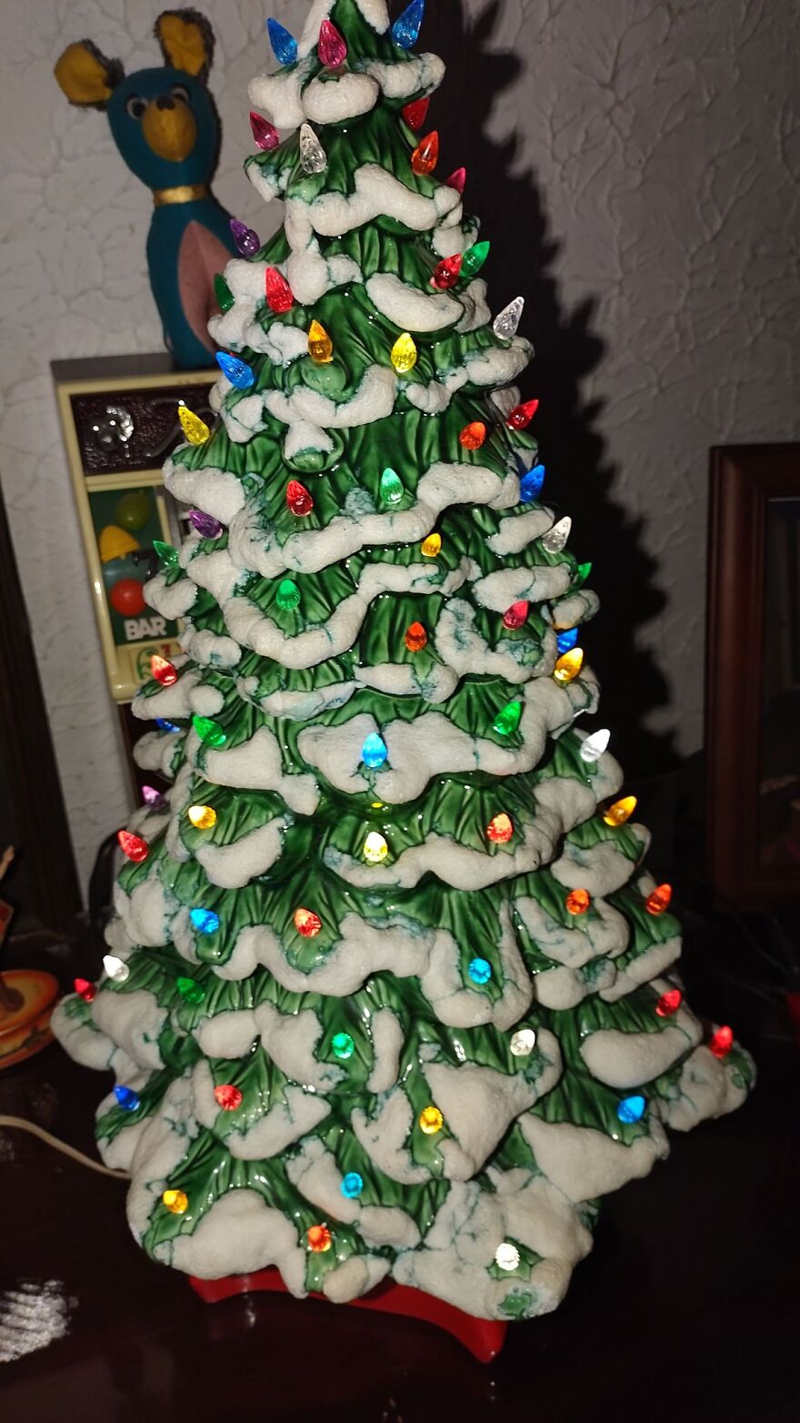 Vintage ceramic Christmas tree decoration with colorful lights and snow-like accents on green branches indoors.