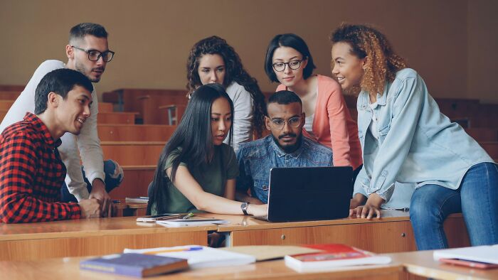 A group of diverse young adults gathered around a laptop, showing emotions linked to feeling betrayed by a best friend.