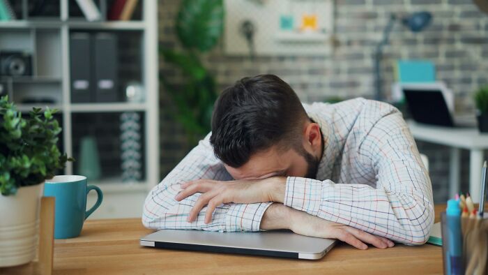 Man resting head on arms over closed laptop showing effects of habits on mental and physical health long-term.