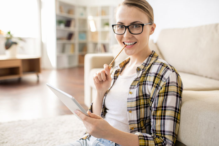 Young woman with glasses sitting on floor using tablet, reflecting on groom ending relationship over debt and wedding costs. Young woman with glasses sitting on floor using tablet, reflecting on groom ending relationship over debt and wedding costs.