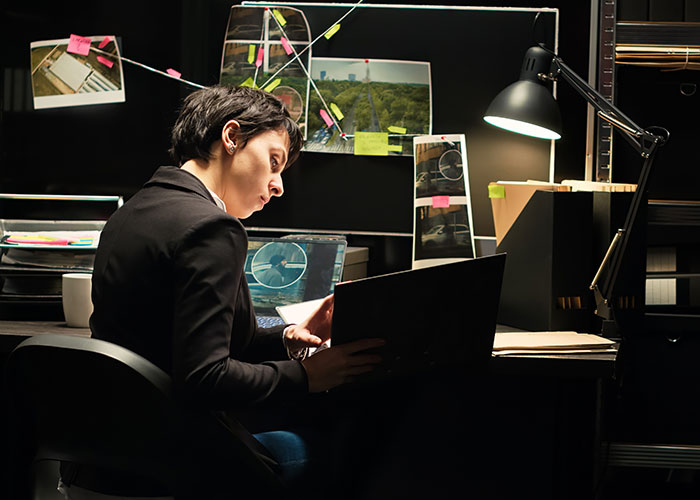 Persona concentrada revisando documentos y pantallas en oficina oscura, ilustrando historias de consecuencias no intencionadas.