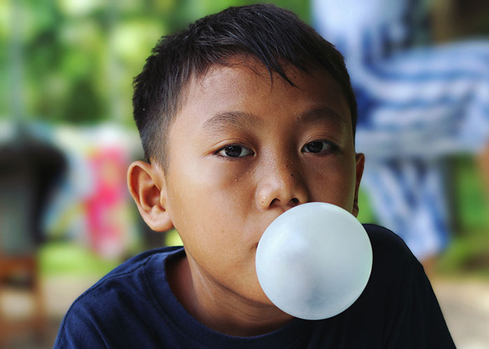 Niño haciendo burbuja con chicle al aire libre, ilustrando historias de consecuencias no intencionadas y celos.