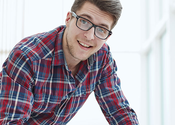 Hombre joven con gafas y camisa de cuadros sonriendo, representando historias de consecuencias no intencionadas.