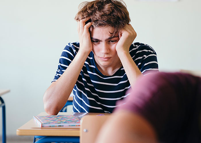 Joven preocupado con camiseta a rayas sentado en salón, reflejando historias de consecuencias no intencionadas y celos.