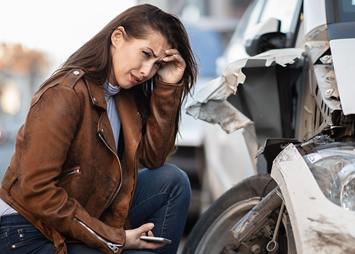 Mujer angustiada junto a su vehículo dañado tras accidente, reflejando consecuencias no intencionadas.