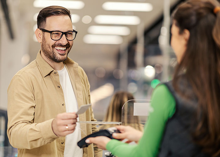 Hombre sonriente pagando con tarjeta en tienda, ilustrando historias de consecuencias no intencionadas y celos inesperados.