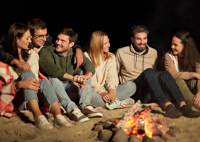 Group of young friends sharing wild cause and effect moments while sitting around a campfire on the beach at night