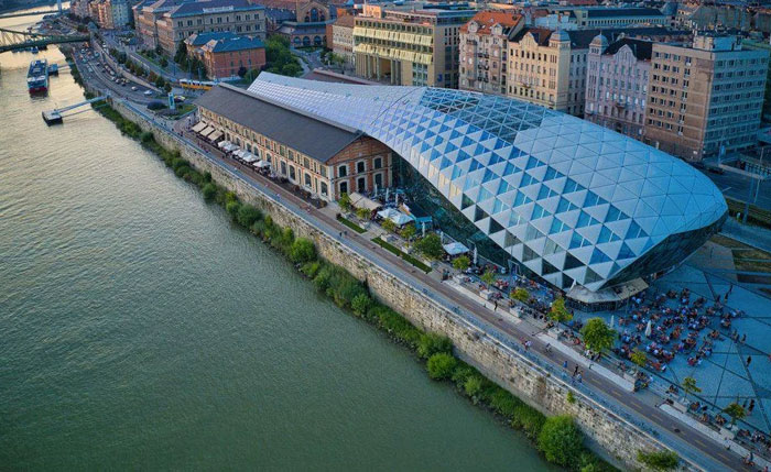 A bread-shaped bread factory building with a modern glass facade located by a riverside in an urban area.