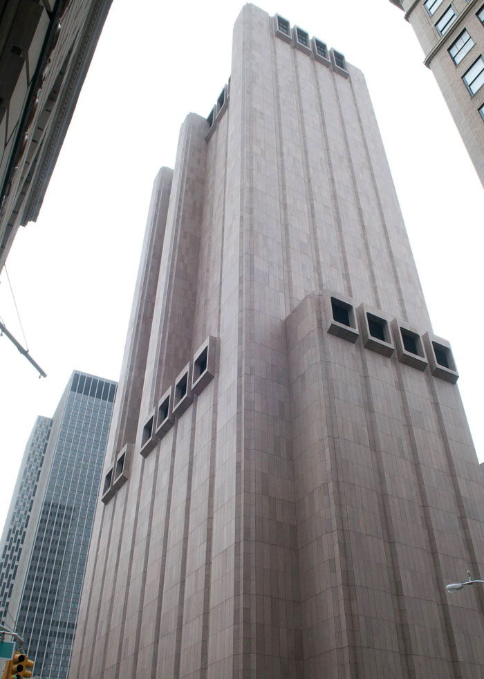 Tall bread-shaped bread factory building with rectangular windows in an urban cityscape among other skyscrapers.