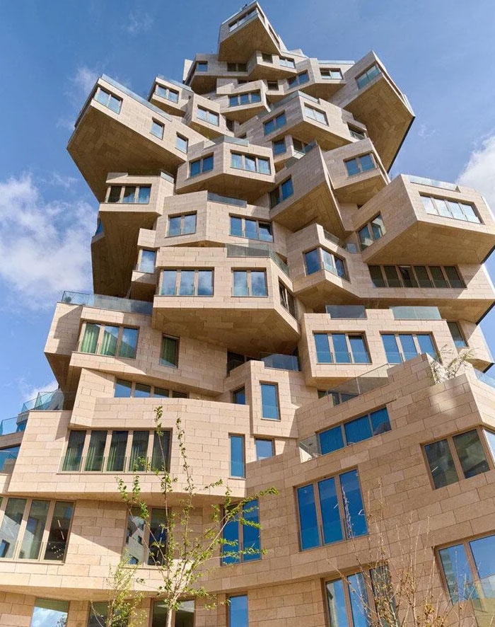 Unique bread-shaped bread factory building with stacked, irregular stone blocks and numerous windows under a clear blue sky.