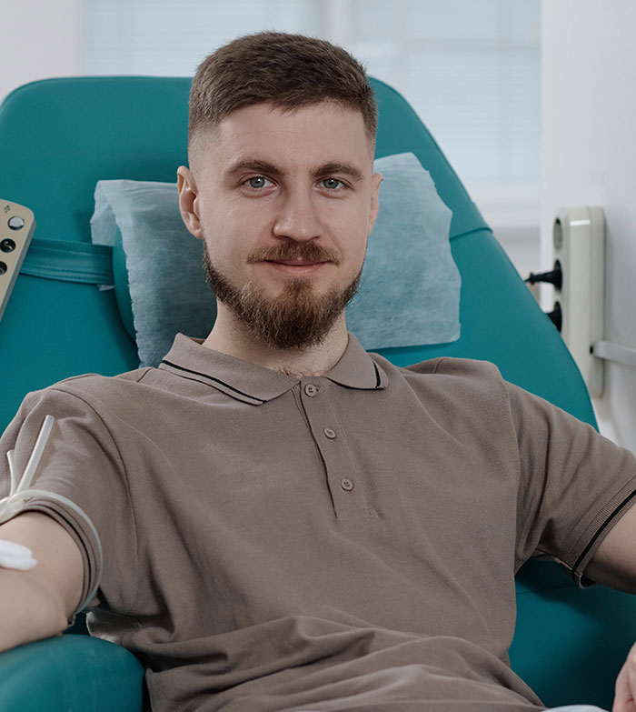 Young man in a medical chair smiling during a DNA test, highlighting shocking family relationship discoveries.