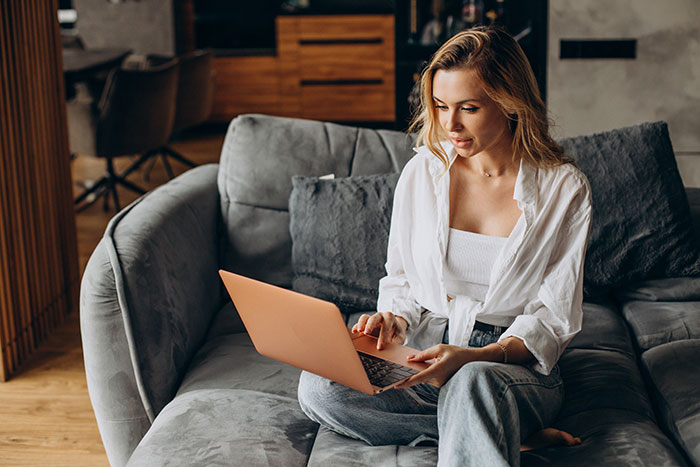 Young woman using a laptop on a couch, researching DNA tests revealing surprising family relationships.