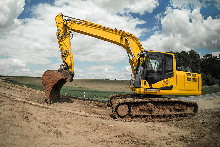 Yellow excavator digging dirt on a construction site under a partly cloudy sky, illustrating unusual excuses for missing work.