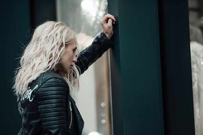 Woman in a leather jacket leaning on a wall looking contemplative, illustrating strange excuses for missing work concept.
