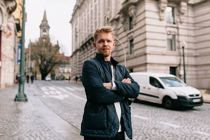Young man standing confidently with arms crossed on a cobblestone street in an urban area, chinchilla ate wallet concept.
