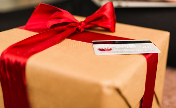 Wrapped gift box with a red ribbon and a credit card, illustrating a white elephant gift refund scenario.