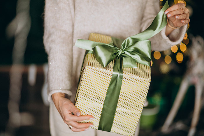 Person holding a wrapped white elephant gift with green ribbon, illustrating a story about stealing and refunding a gift.