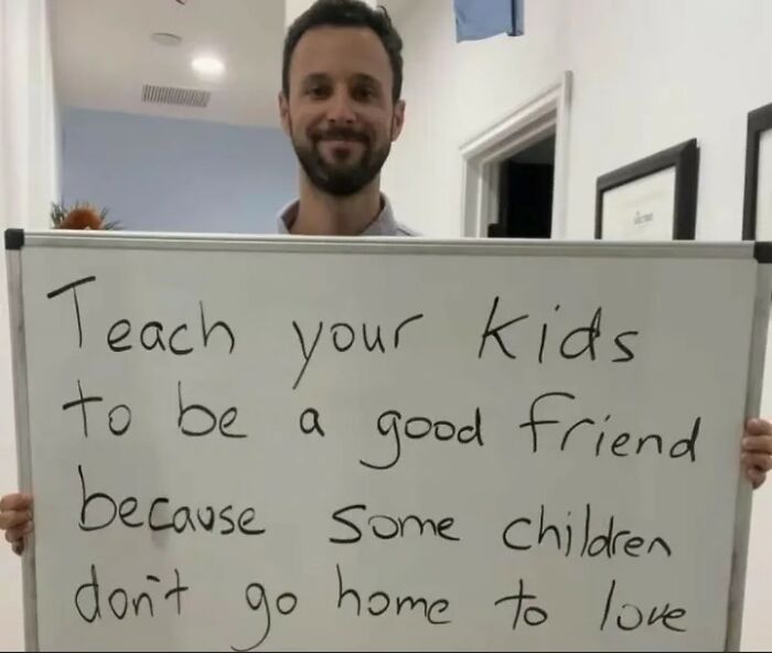 Man holding whiteboard with message about teaching kids to be good friends, a sweet and wholesome pic to cleanse your feed.
