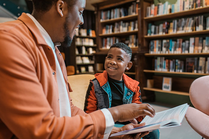 Father and son reading a book together in a library, highlighting a mom furious over teacher's inappropriate note controversy.
