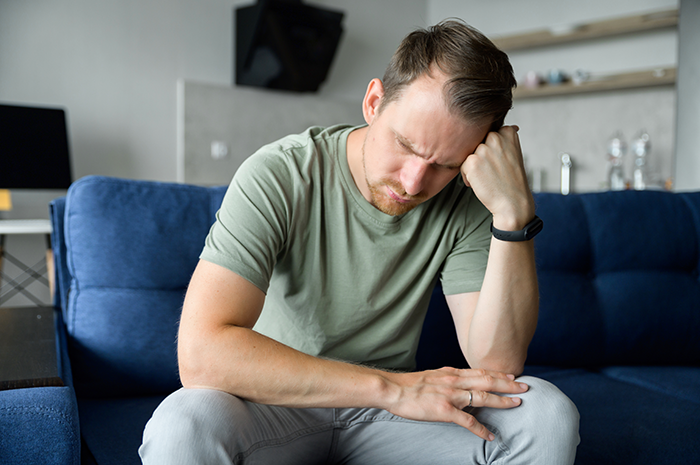 Man sitting on couch looking distressed, representing family tension and transphobic issues after son's coming out. Man sitting on couch looking distressed, representing family tension and transphobic issues after son's coming out.