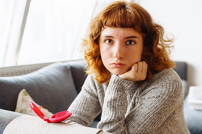 Young person with red hair and gray sweater looking serious, reflecting on family struggles after coming out and facing transphobia. Young person with red hair and gray sweater looking serious, reflecting on family struggles after coming out and facing transphobia.