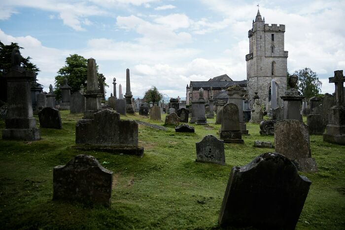 Ancient cemetery with weathered gravestones and a stone church tower, evoking mysteries we aren’t close to solving.