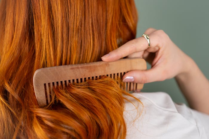 Woman gently detangling daughter&rsquo;s friend&rsquo;s long red hair with a wooden comb in a close-up view