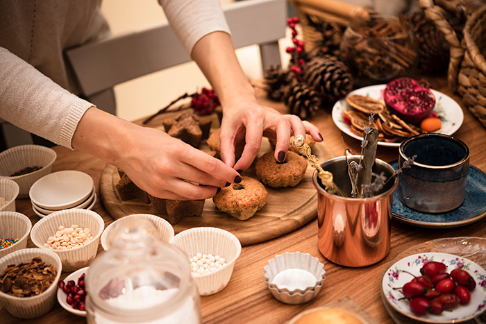 Hands of a woman preparing Christmas treats surrounded by festive decorations highlighting moms doing all the labor during holidays