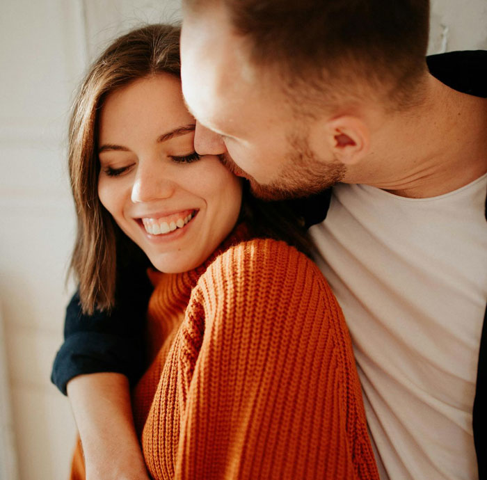 Woman smiling while man affectionately kisses her, illustrating themes of proof and cheating in relationships.