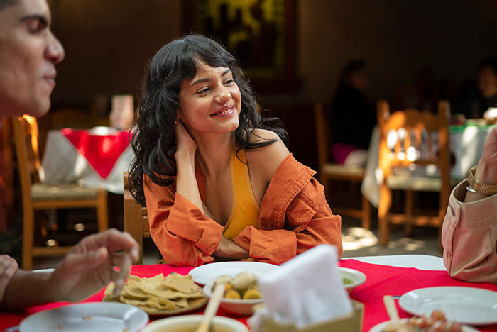 Woman smiling at a family gathering, with future in-laws discussing a prenup after learning about her wealthy background.