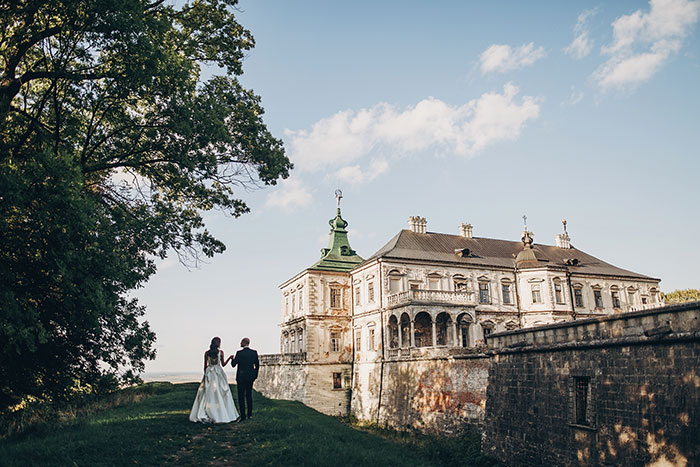 Bride and groom walking near a historic mansion, illustrating future in-laws' demand for prenup amid wealthy family background.