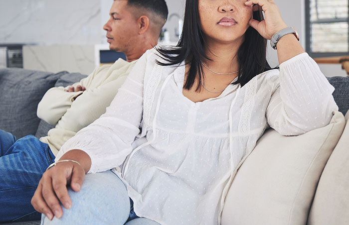 Couple sitting apart on couch in silence, depicting tension after lottery winner refuses to share prize with girlfriend.