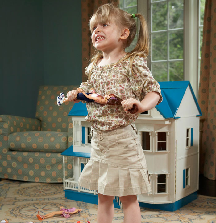 Young girl displaying aggressive behavior, holding dolls roughly, illustrating stepdaughter&rsquo;s difficult behavior concerns.