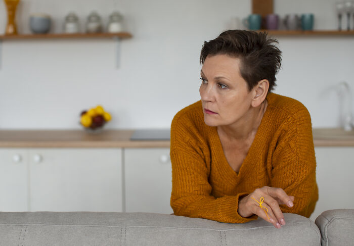 Middle-aged woman in orange sweater looking concerned in a modern kitchen, reflecting family tension over vegan teen diet.
