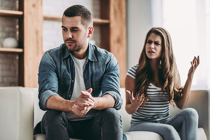 Woman looks upset while fianc&eacute; sits silently on couch worried about their wedding photos and appearance.