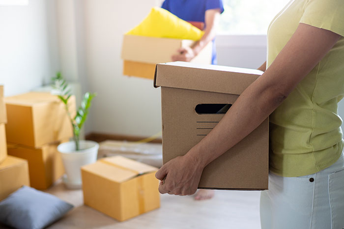 Woman holding a moving box inside a home filled with packed boxes, relating to secret texts and wedding photo worries.
