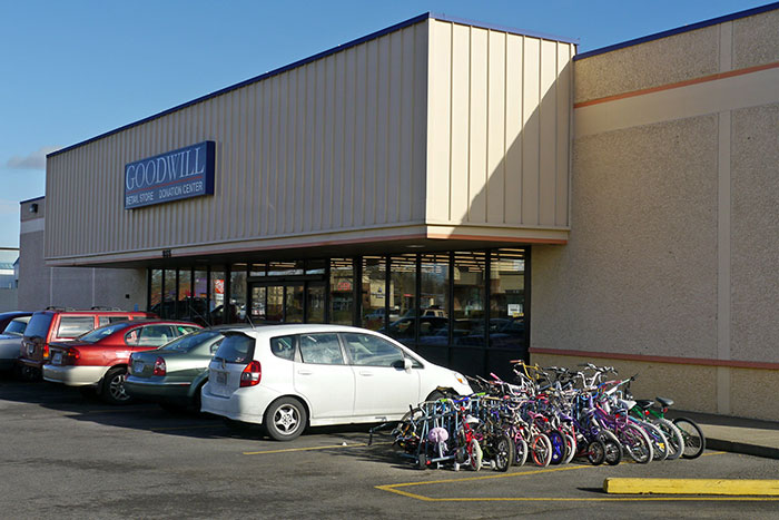 Goodwill store exterior with parked cars and bicycles, setting for older man and younger generations discussion.