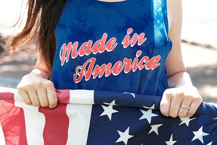 Woman wearing made in America tank top holding folded American flag outdoors on a sunny day
