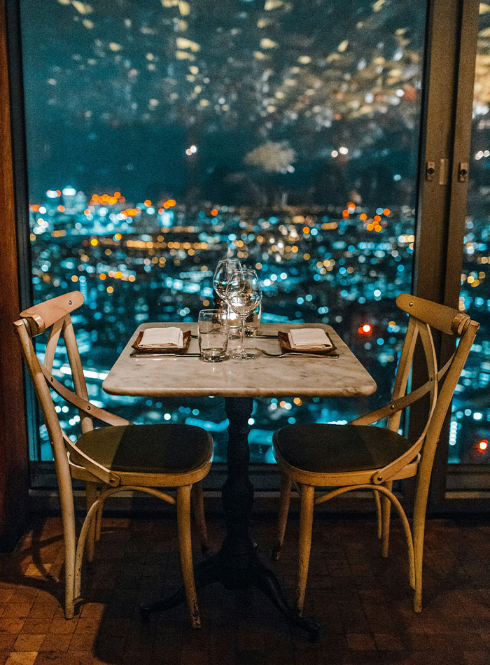 Romantic dinner table set for two with glasses and napkins overlooking a city nightscape, reflecting a jerk dating scenario.