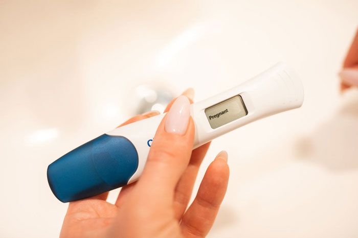 Hand holding a positive pregnancy test, relating to uncertainty about affair partner's baby and family relationships.