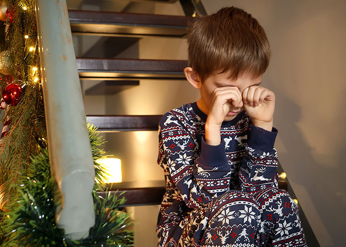 Young boy in festive pajamas sitting on stairs rubbing eyes, conveying emotions related to mom running away from her kids on Christmas.