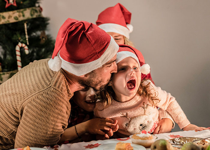 Family wearing Santa hats during Christmas celebration, capturing candid moments of kids and parents sharing holiday joy.