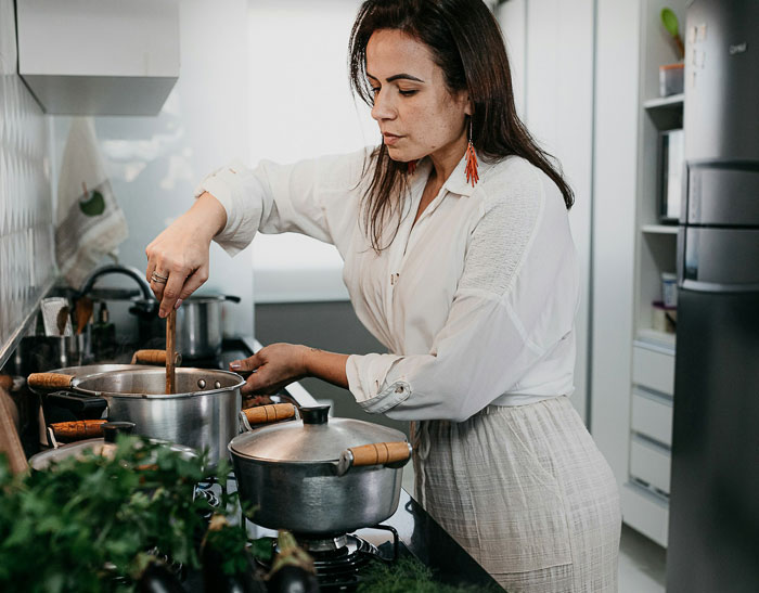 Woman cooking in kitchen stirring pots on stove preparing cooked lunches with focused expression