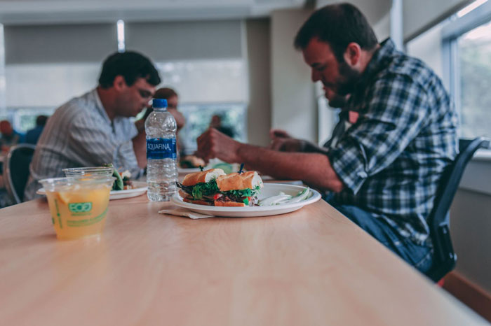 Man upset at lunch table with cooked sandwiches while others eat, reflecting woman upset boyfriend throwing away cooked lunches.