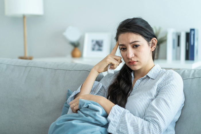 Upset woman sitting on couch holding a blanket, reflecting the emotion of a woman upset boyfriend throwing away cooked lunches.