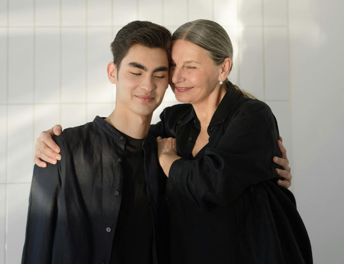 Woman smiling warmly while hugging her son, symbolizing being blinded by flowers, unaware of daughter&rsquo;s efforts.